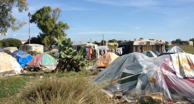 Capanne costruite nel fango, con teli di plastica e pezzi di legno, immondizia ovunque e uno spesso fumo nero che proviene dai fuochi accesi su vecchie lastre di eternit. Non c’è acqua e non c’è un bagno, non c’è un’infermeria e non ci sono medicinali: solo piccoli serbatoi che non potranno mai soddisfare l’approvvigionamento idrico, tra tanti insetti, pidocchi e sporcizia. Non è un accampamento di profughi e non siamo nella periferia di una città africana, non è un campo di concentramento e qui le guerre e i bombardamenti sono lontani chilometri. Siamo invece aCampobello di Mazara, comune siciliano in […]